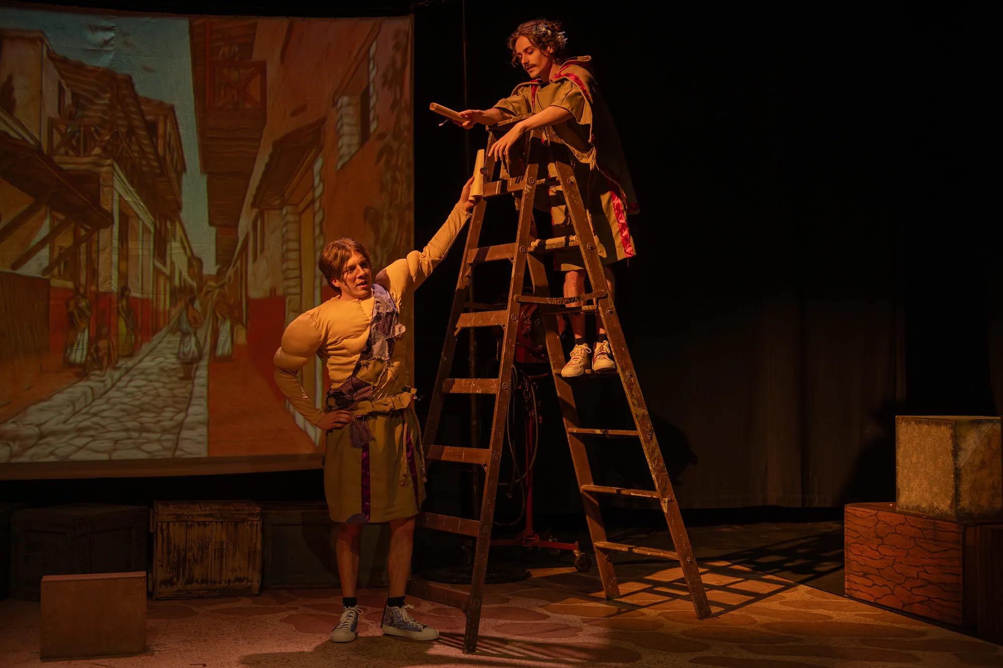 An actor climbs a ladder toward a performer at the top