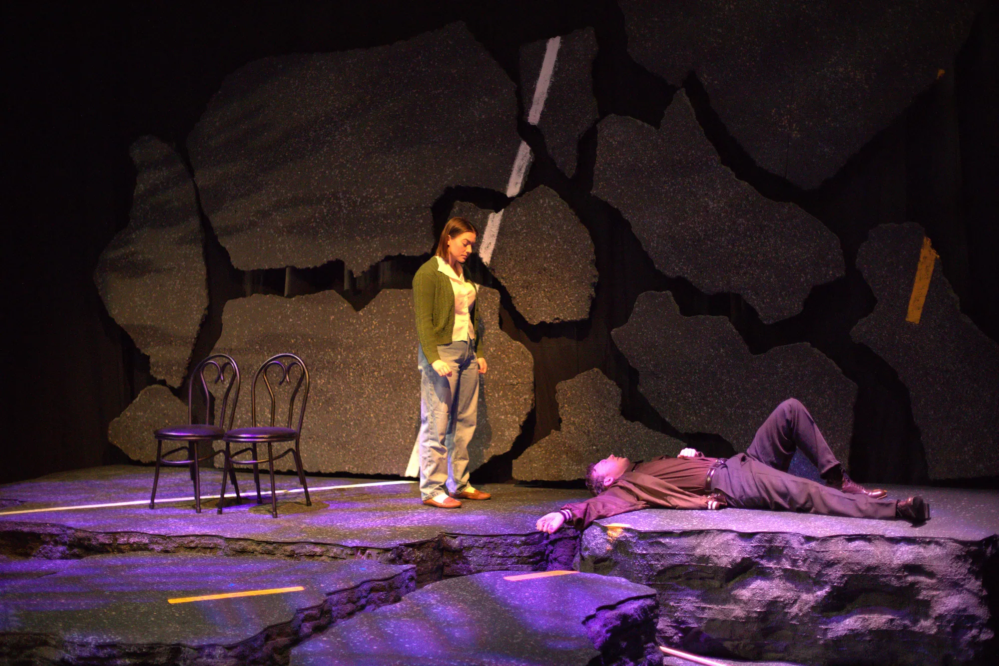 A woman stands over a man lying on the rock-strewn road