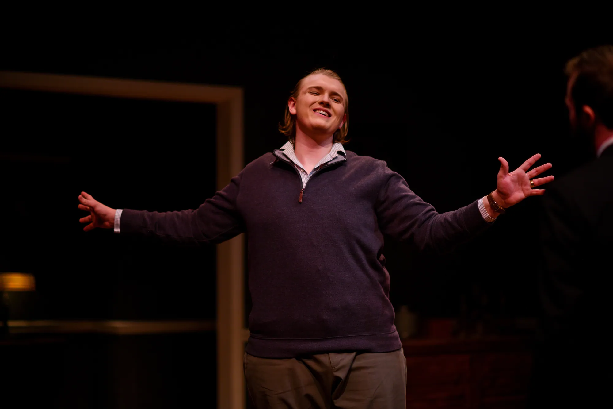 A man flings his arms wide, grinning, in a pool of light