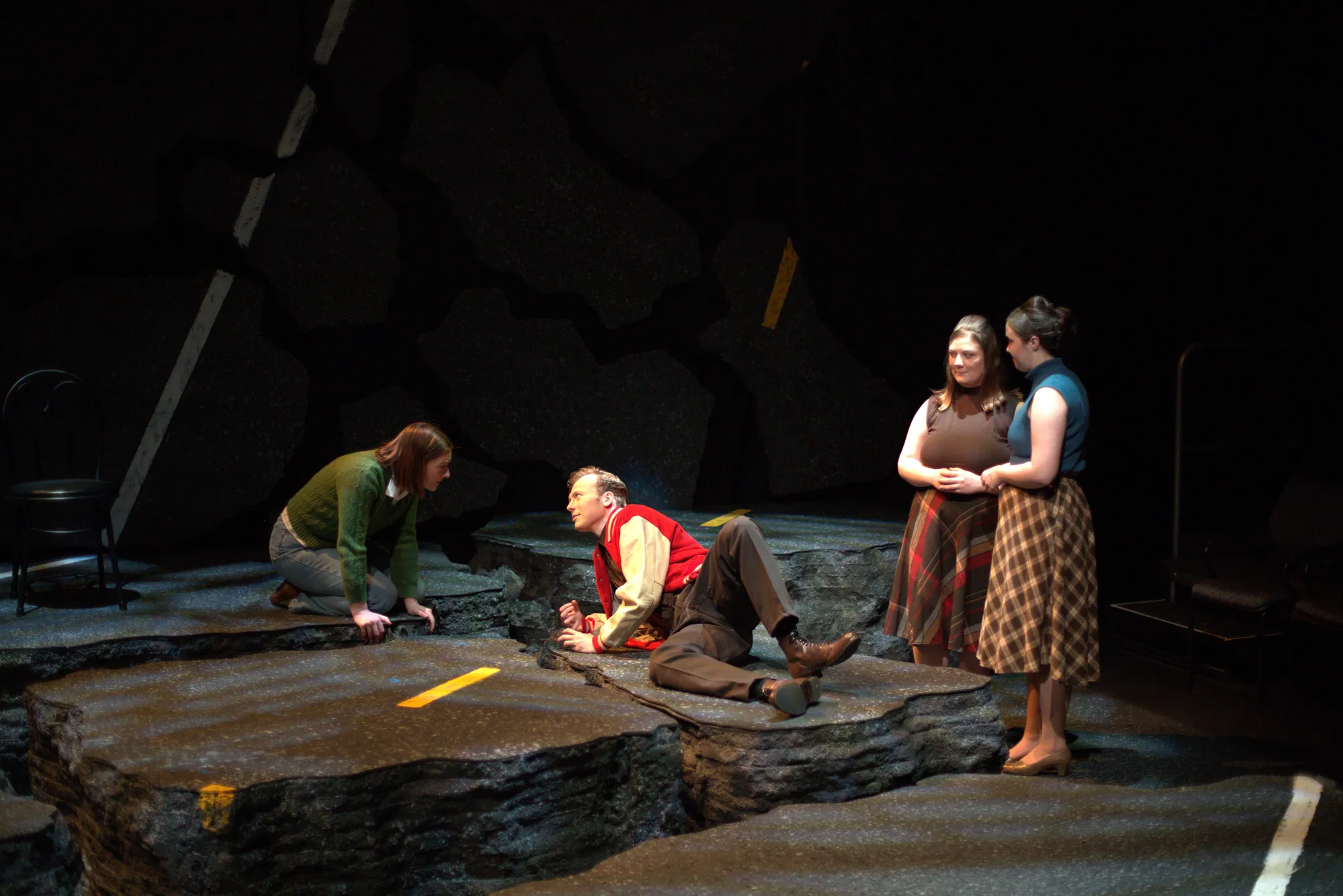 The chorus gathers around a fallen man on the broken road