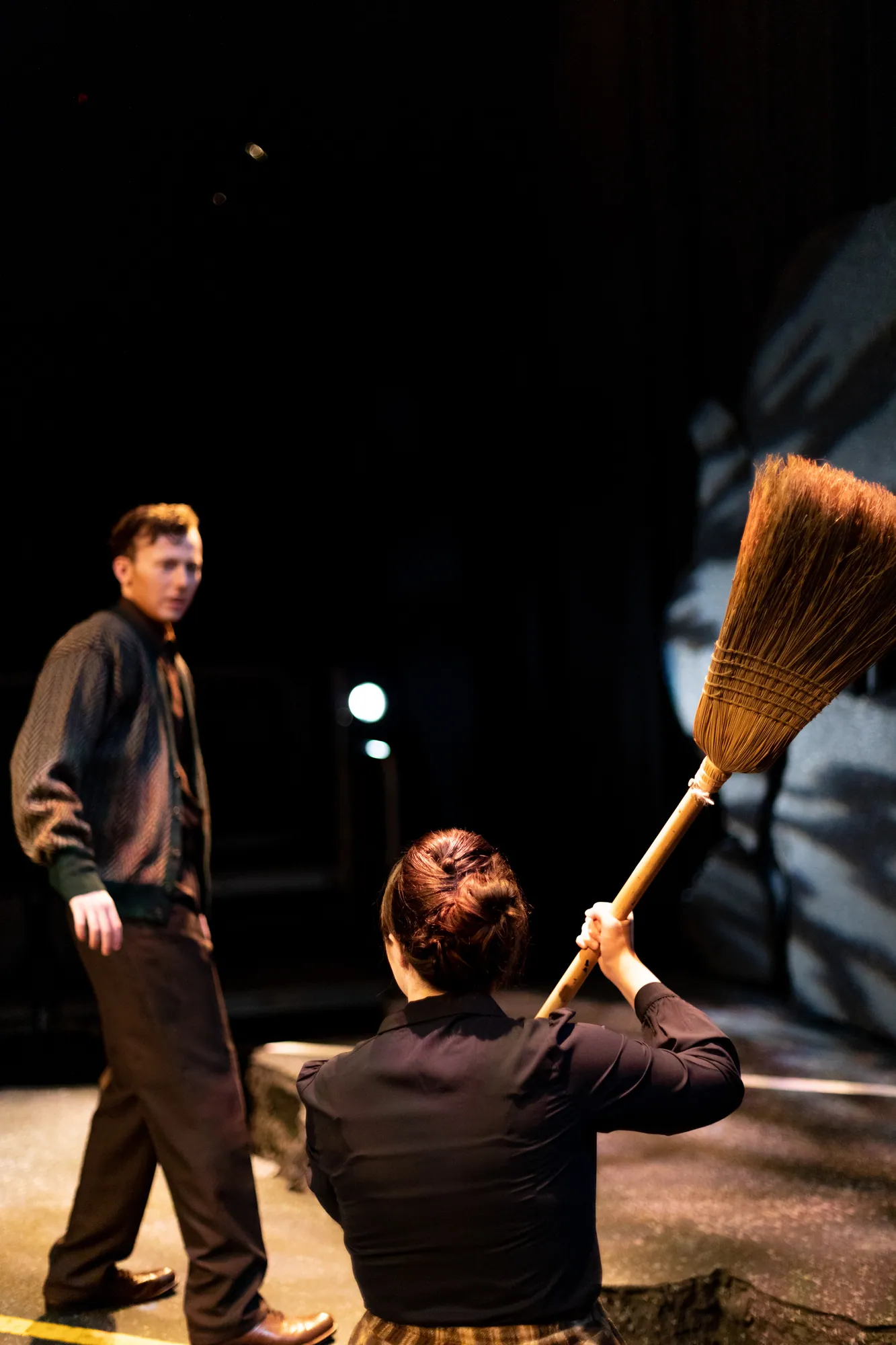 A figure raises a broom over a seated man