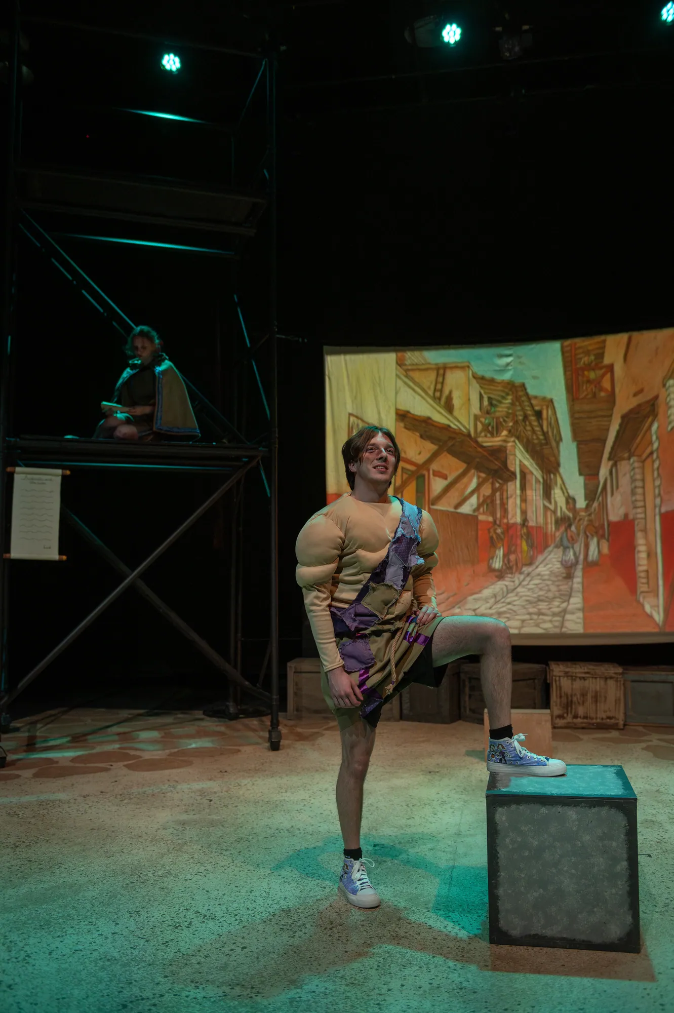 A performer stands on a crate beside the scaffolding