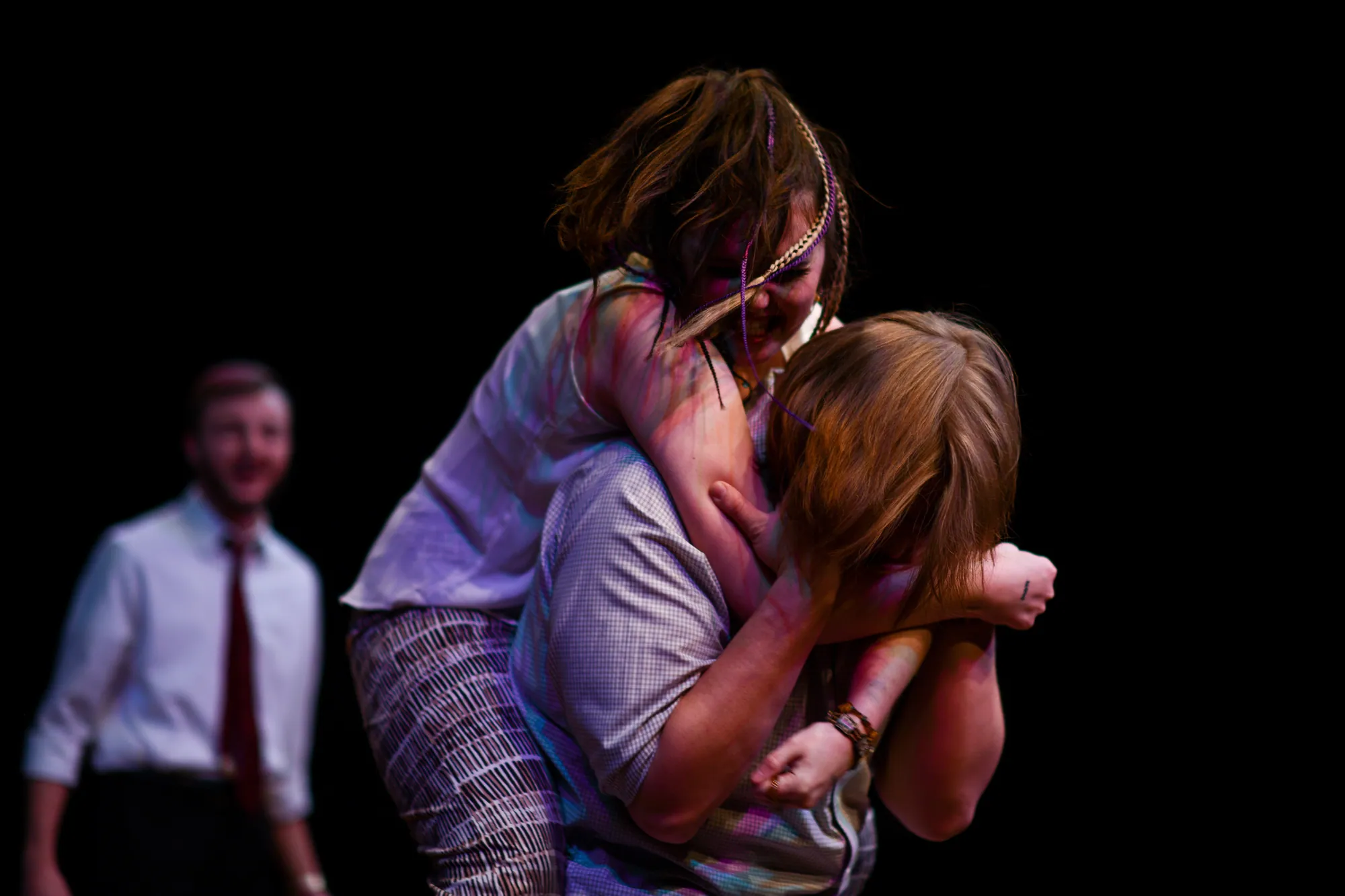 One woman clings to another’s back while a man watches