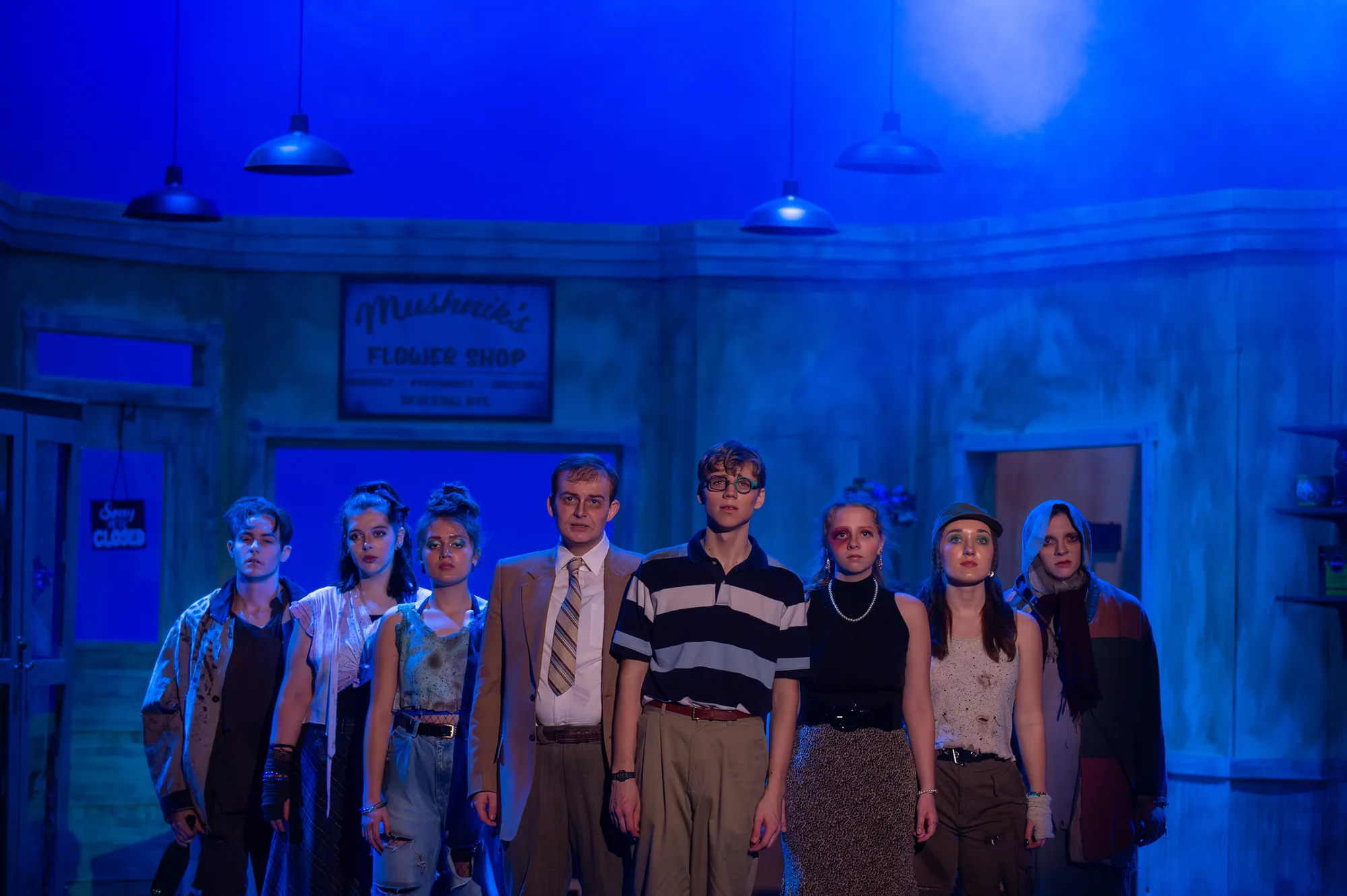 The full company stands together in blue light