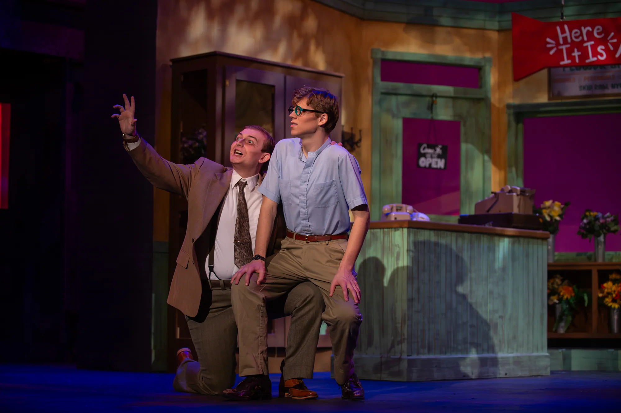 Two men seated on the shop floor, one with an arm thrown up mid-song