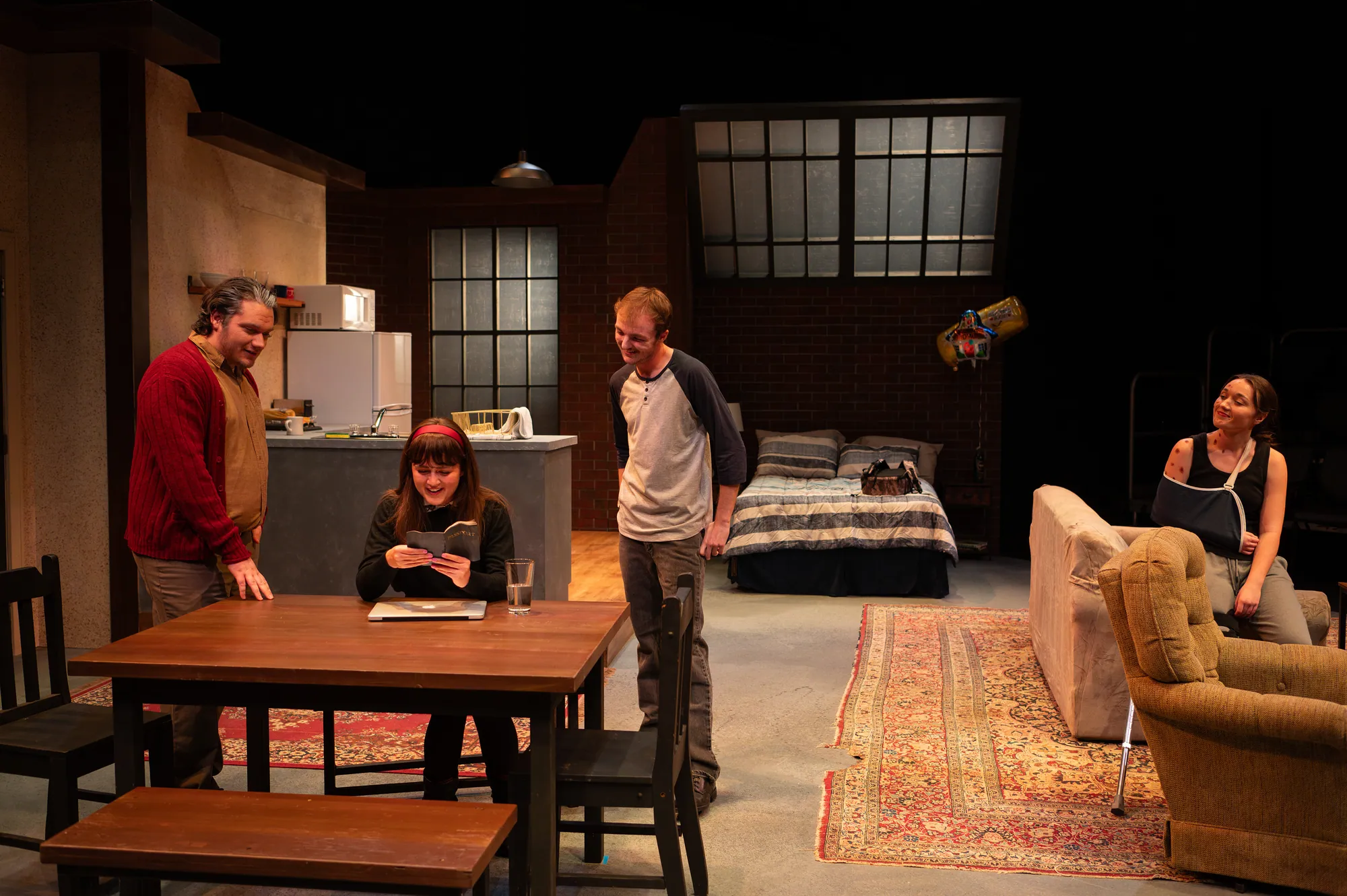 Four actors spread across a loft apartment set with a kitchen and dining table