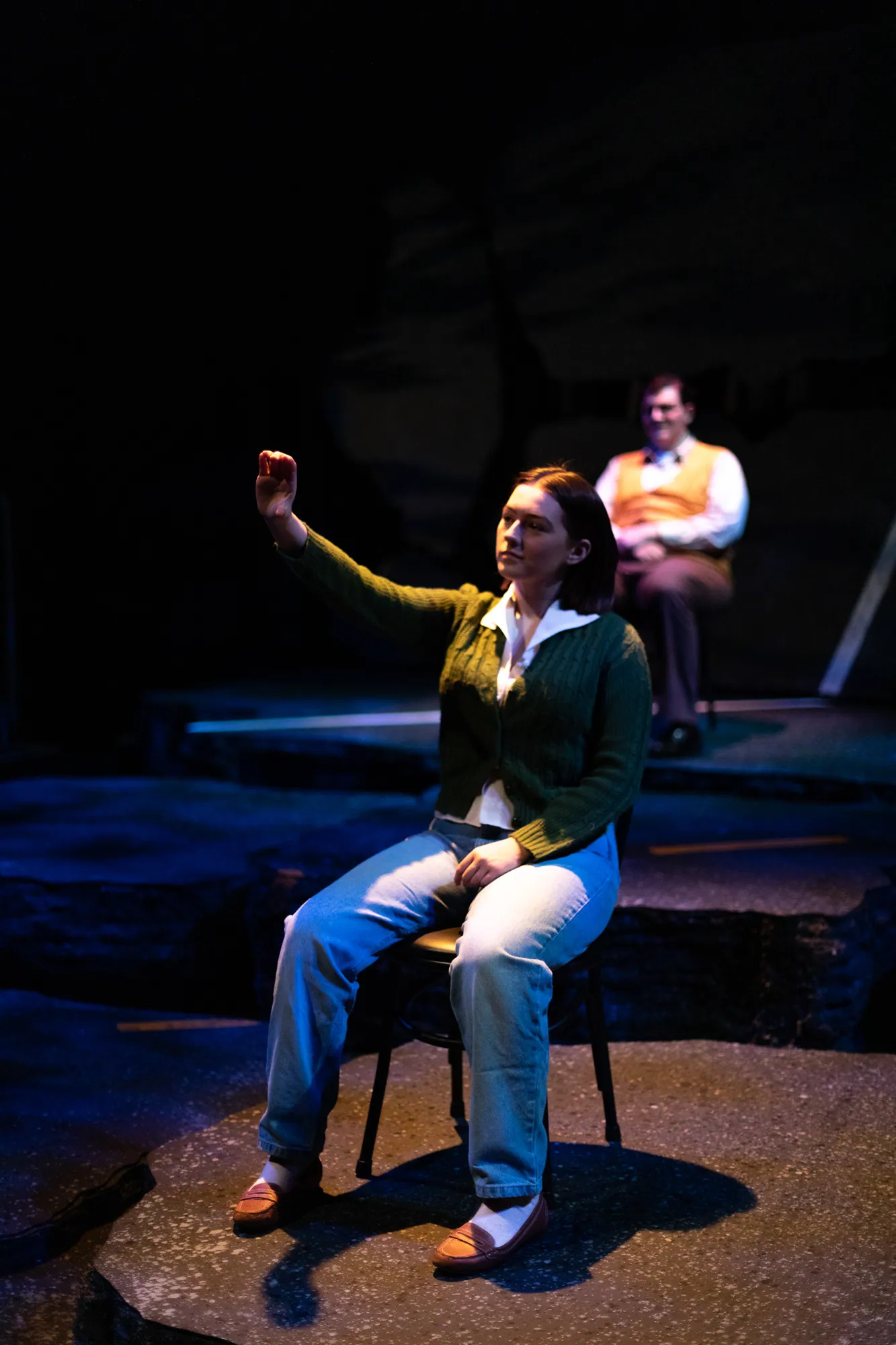 A woman seated alone in a single chair, lit in blue