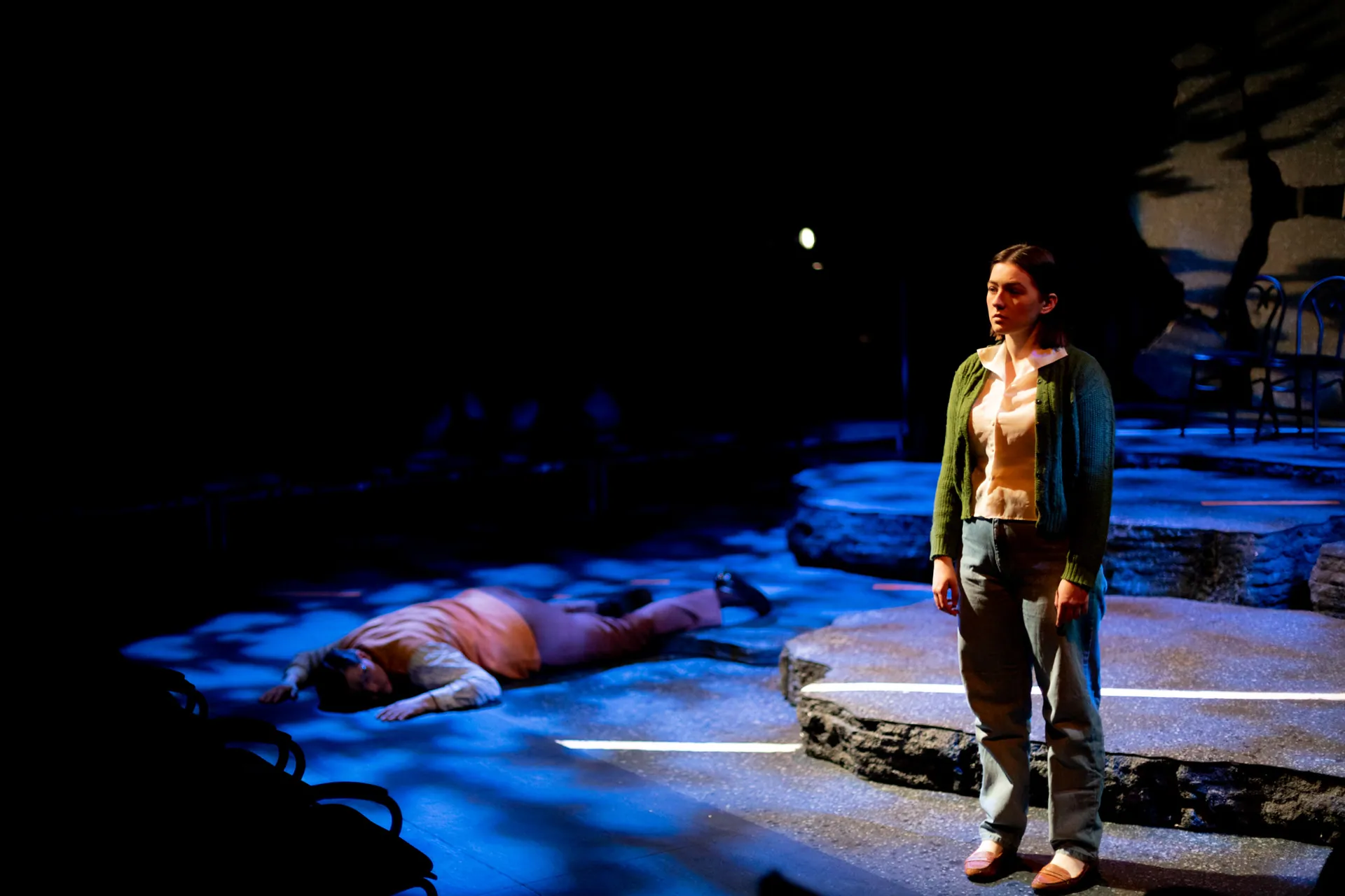 A young woman stands in blue light beside a fallen figure on a broken highway — How I Learned to Drive, directed by Jim Harris